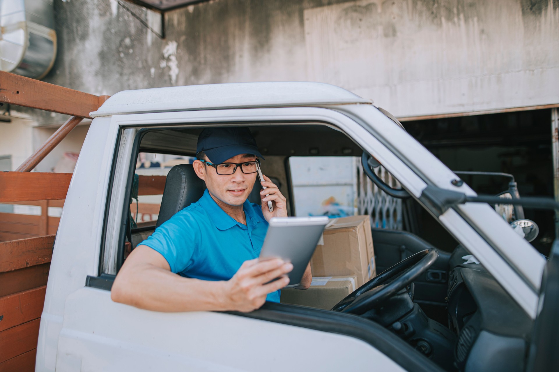 asian chinese mature male delivery person communicating with his customer using phone at driver's seat inside delivery van