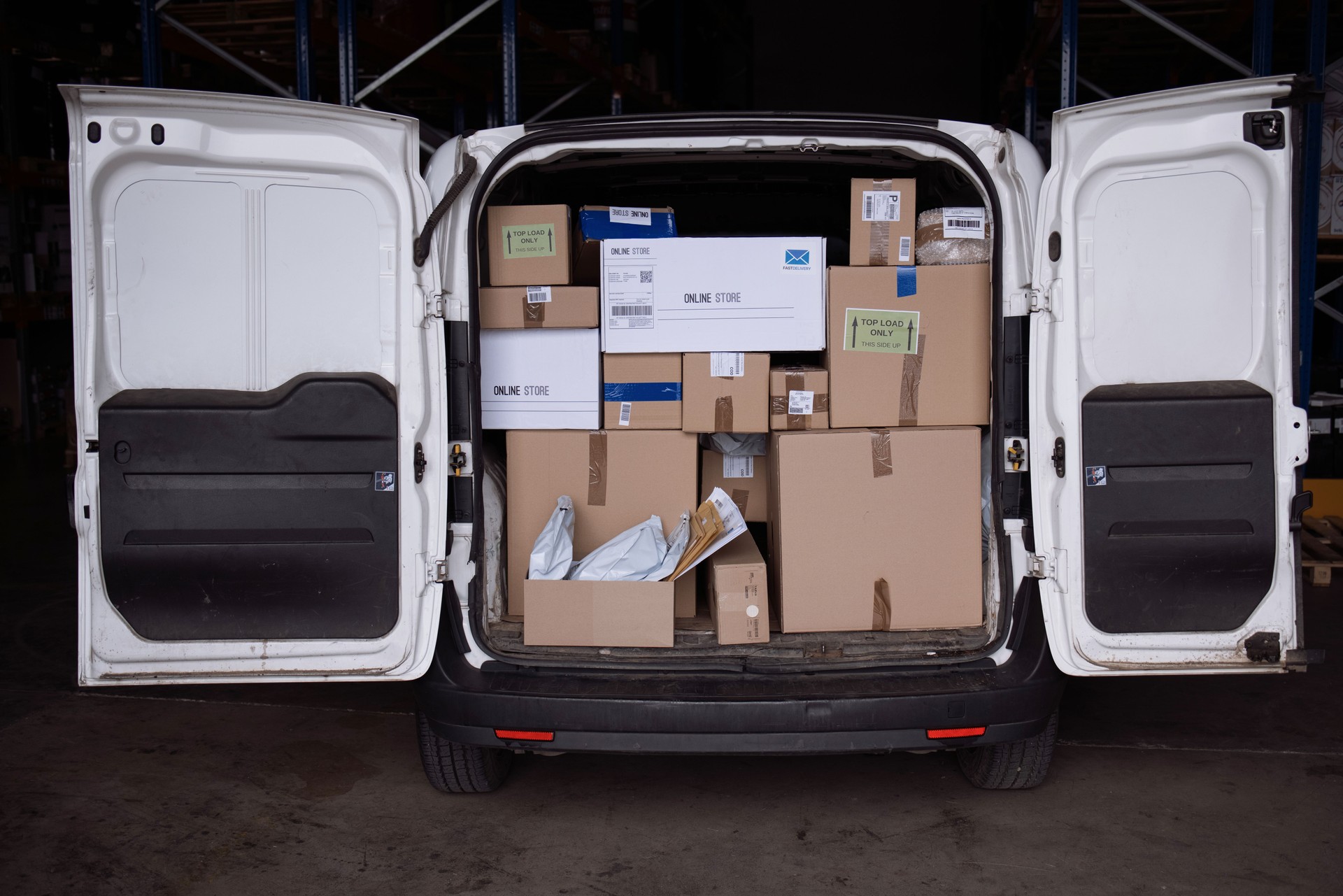 Delivery man working on digital tablet while organising packages for shipment in a van with his coworker.